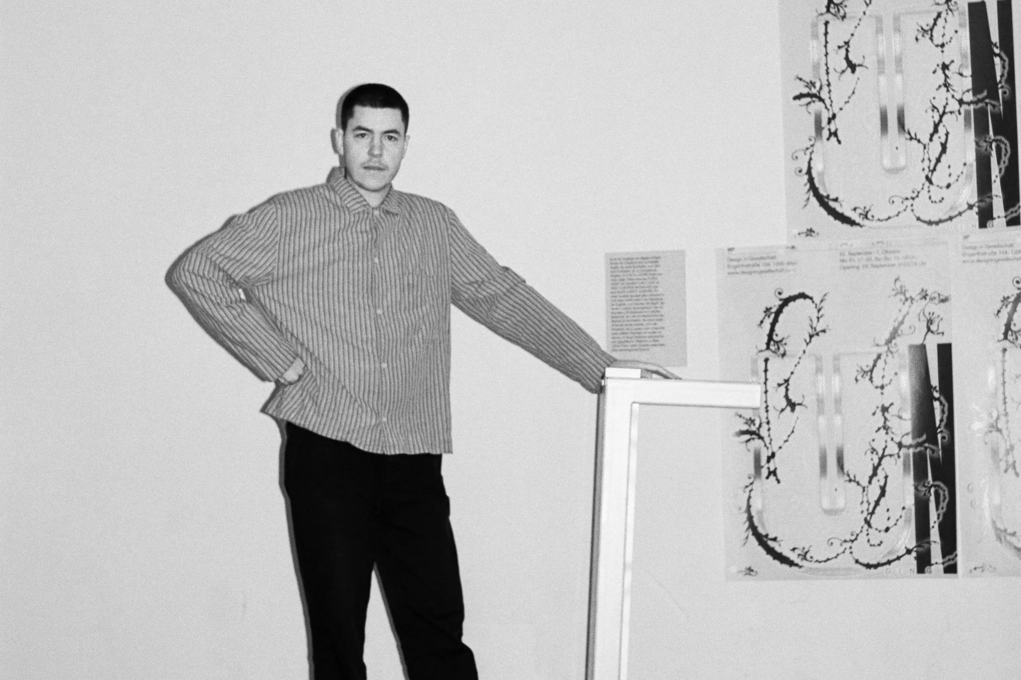 Man in striped shirt standing next to illustrations on wall