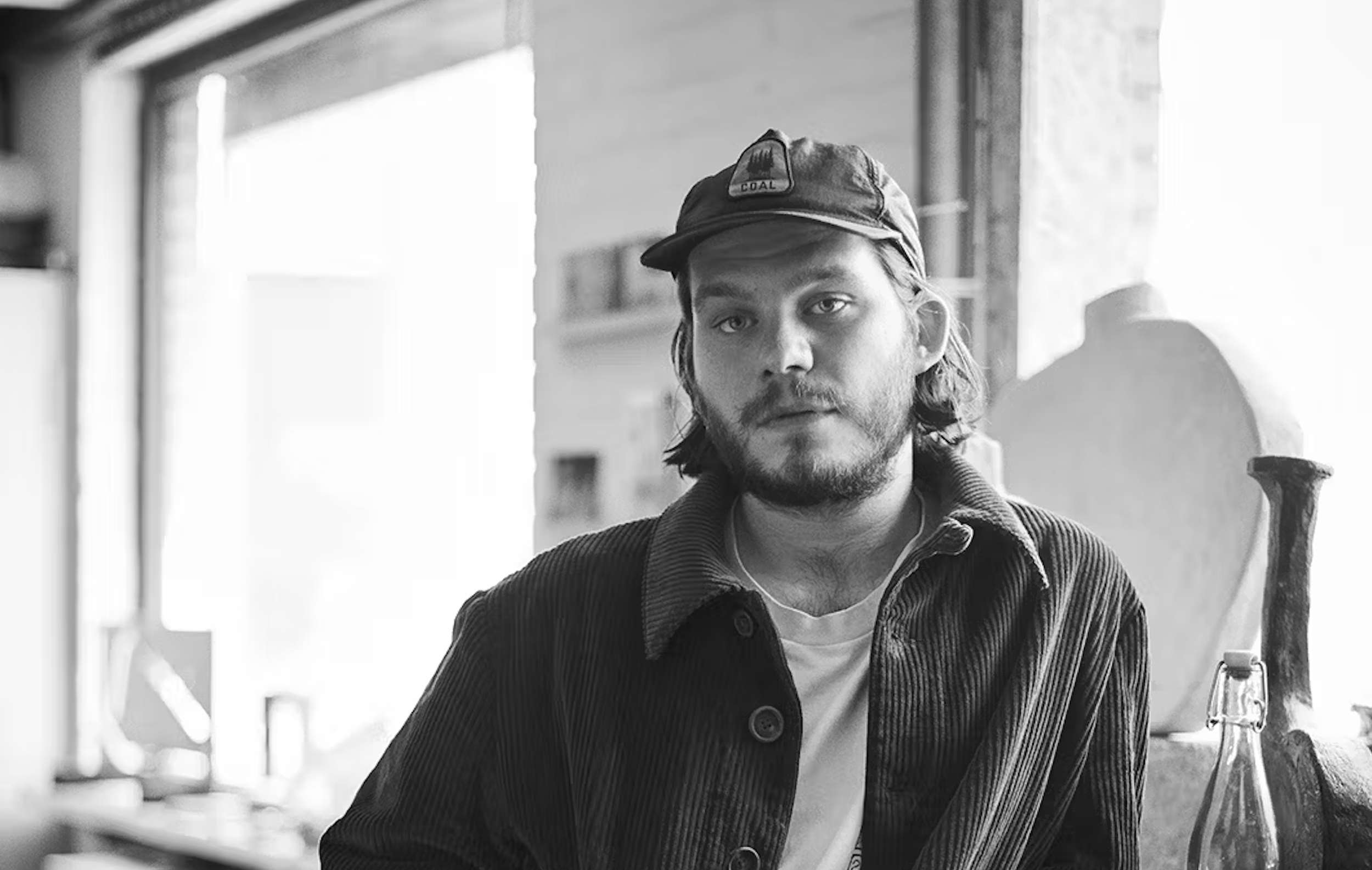 Black and white portrait of a man wearing a cap indoors.
