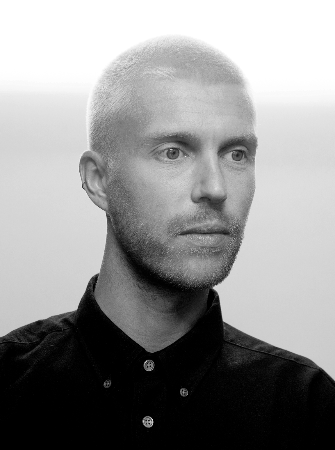 Black and white portrait of a person with short hair wearing a buttoned shirt, facing slightly to the right.