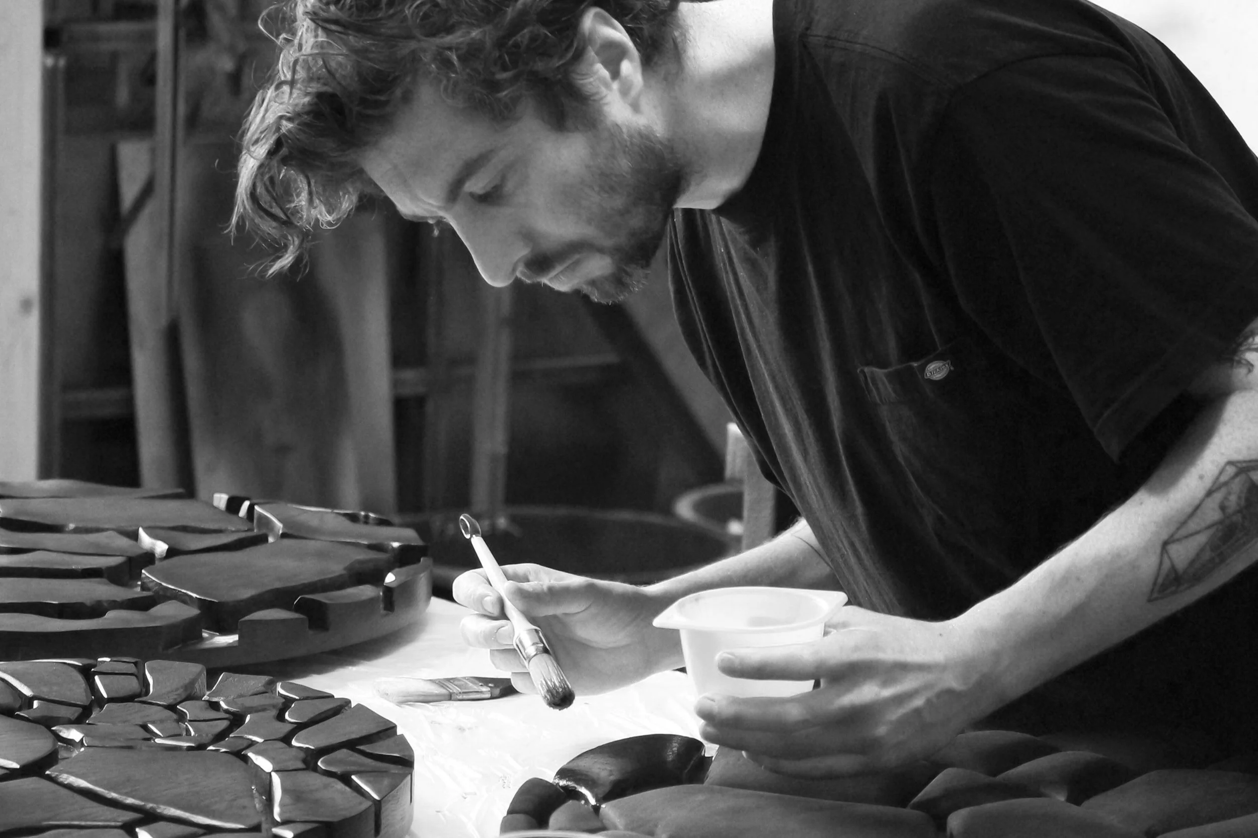 Artist painting a wooden sculpture with a paintbrush and a container of paint in a workshop.