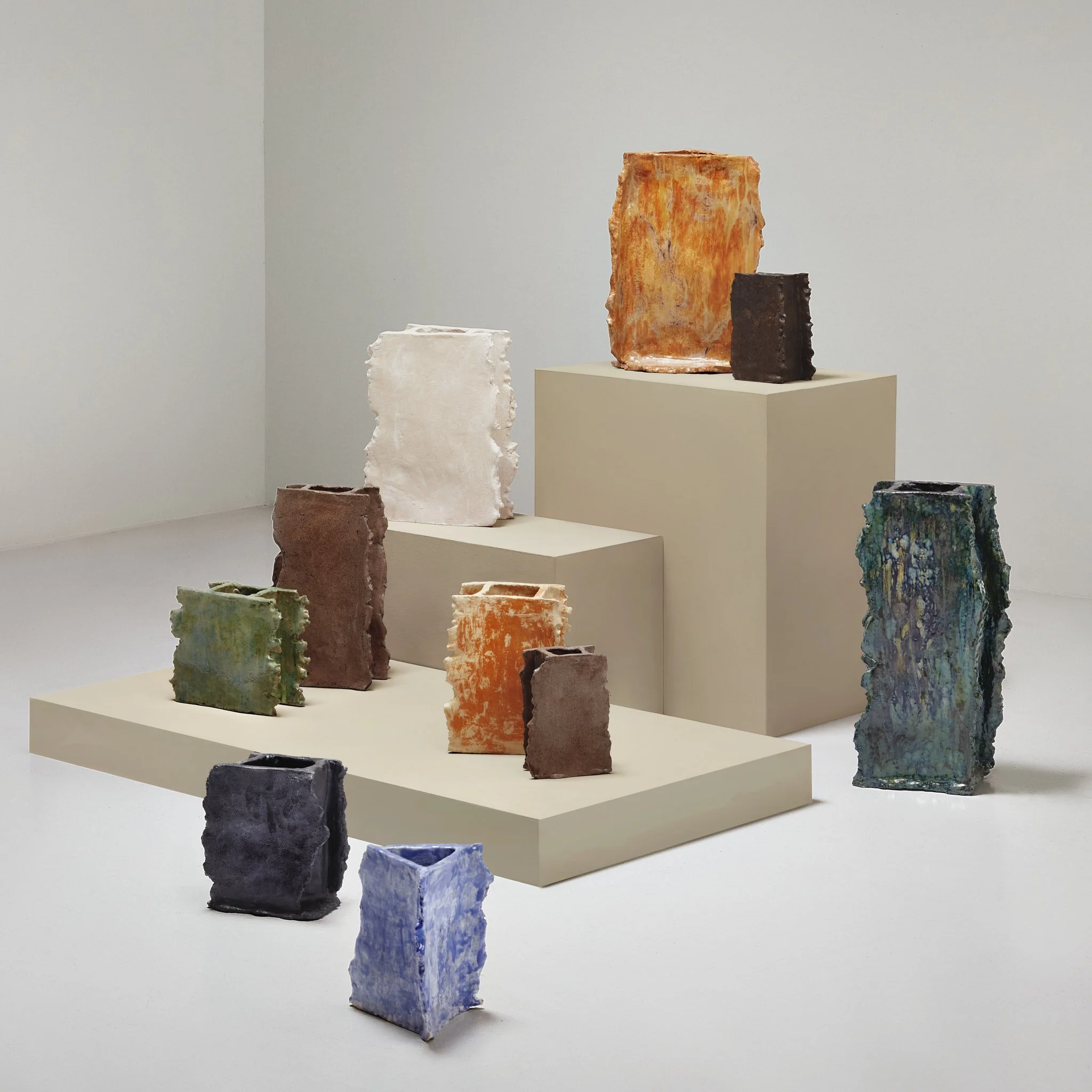 Assortment of textured ceramic vases in various colors displayed on beige platforms.