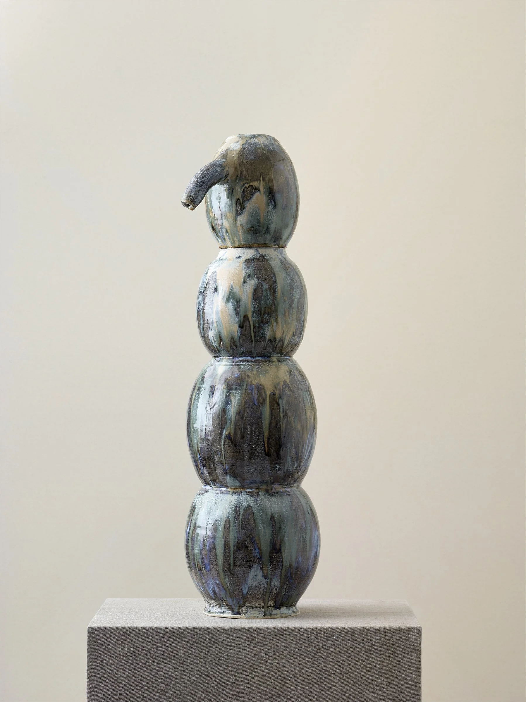 Sculpture with four stacked spherical forms, dark glaze finish, on pedestal.