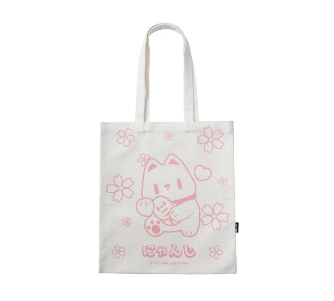 White tote bag with pink illustration of a cute character holding a fish, surrounded by cherry blossom flowers and a small heart, with Japanese characters at the bottom.