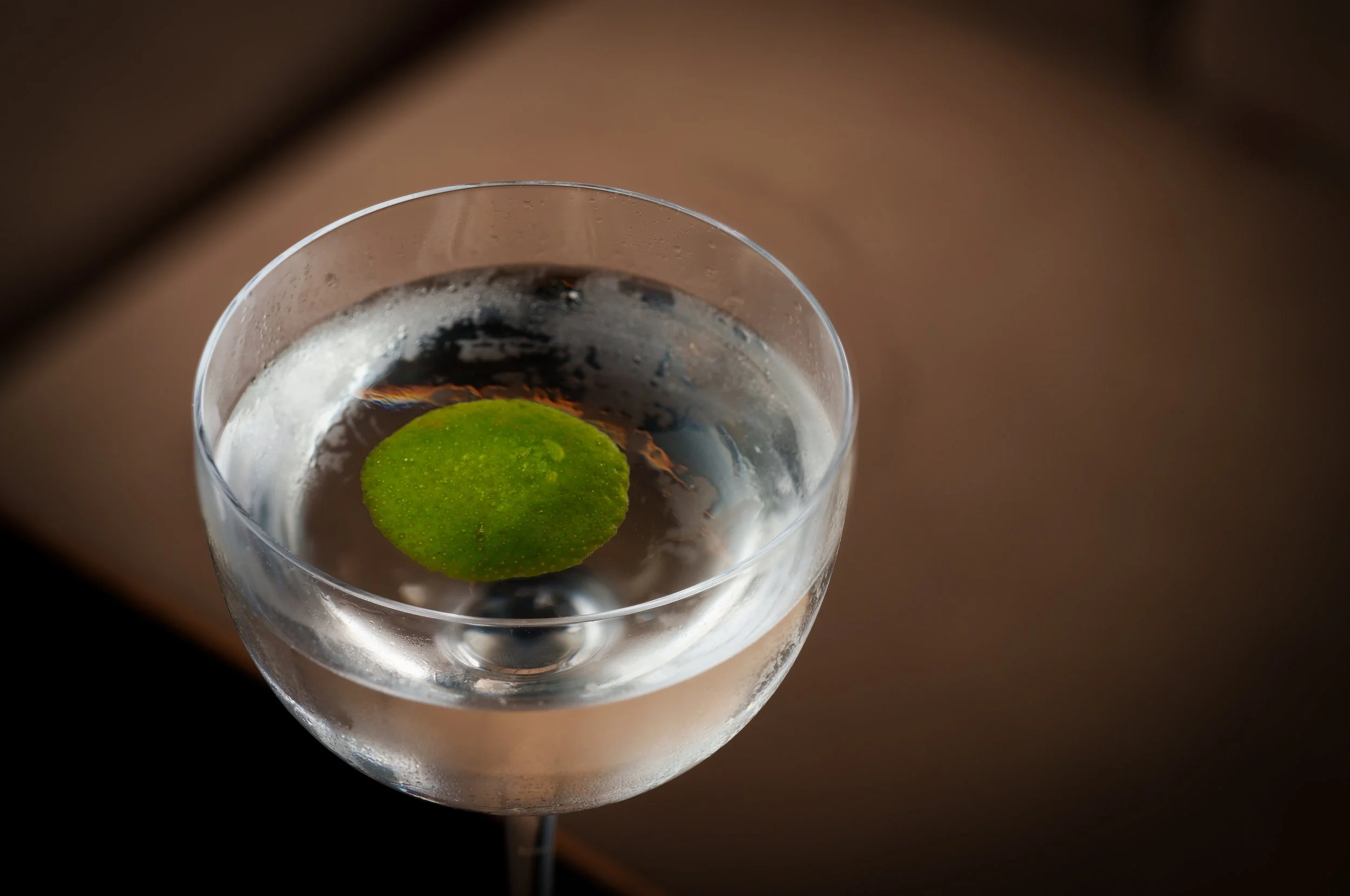 A cocktail with a green lime slice and a dark blueberry garnish in a clear glass.