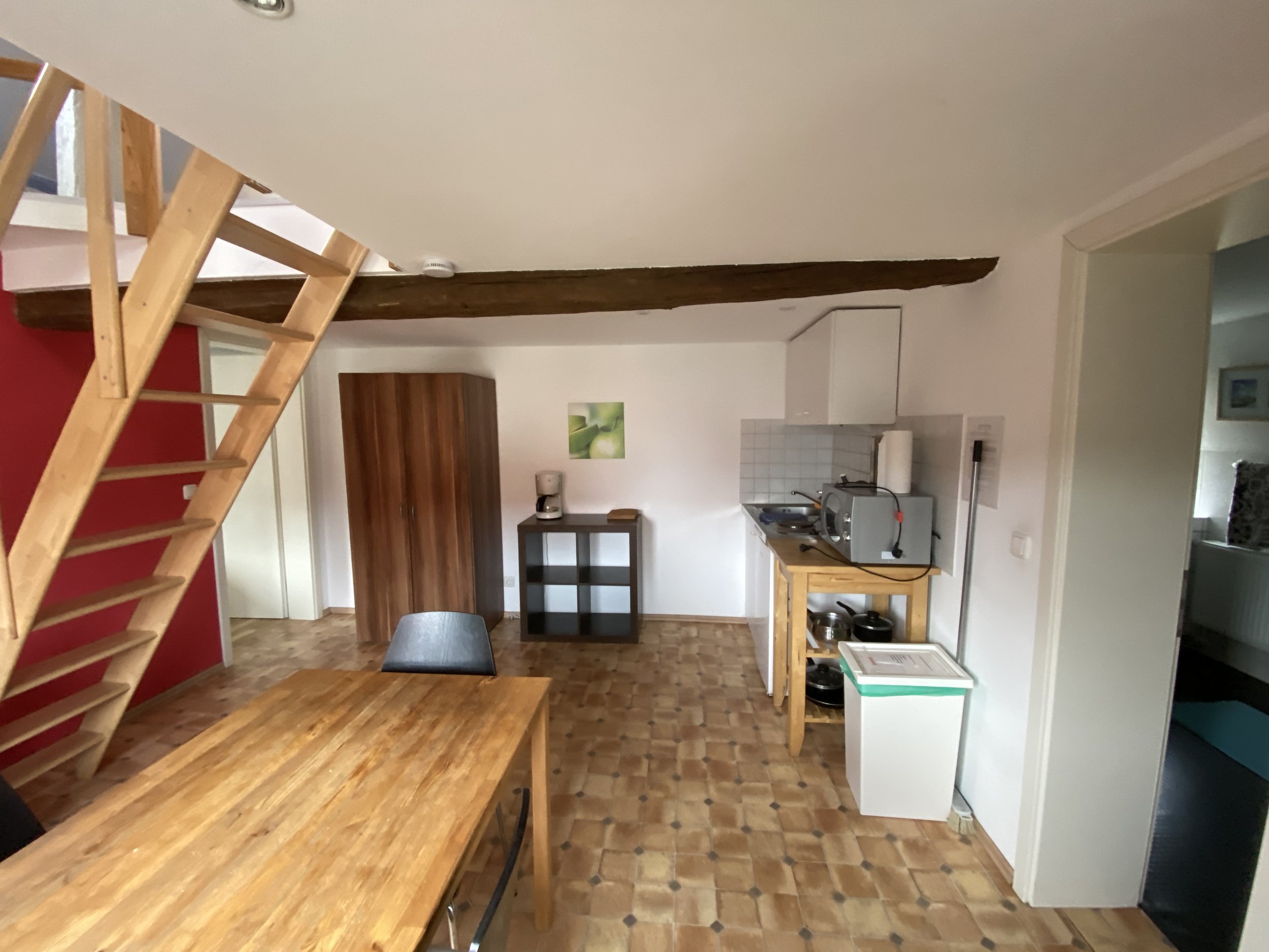 Küchen- und Essbereich in einer Wohnung mit Holztisch, schwarzen Stühlen, Küchenzeile und Offene Treppe zum Obergeschoss.