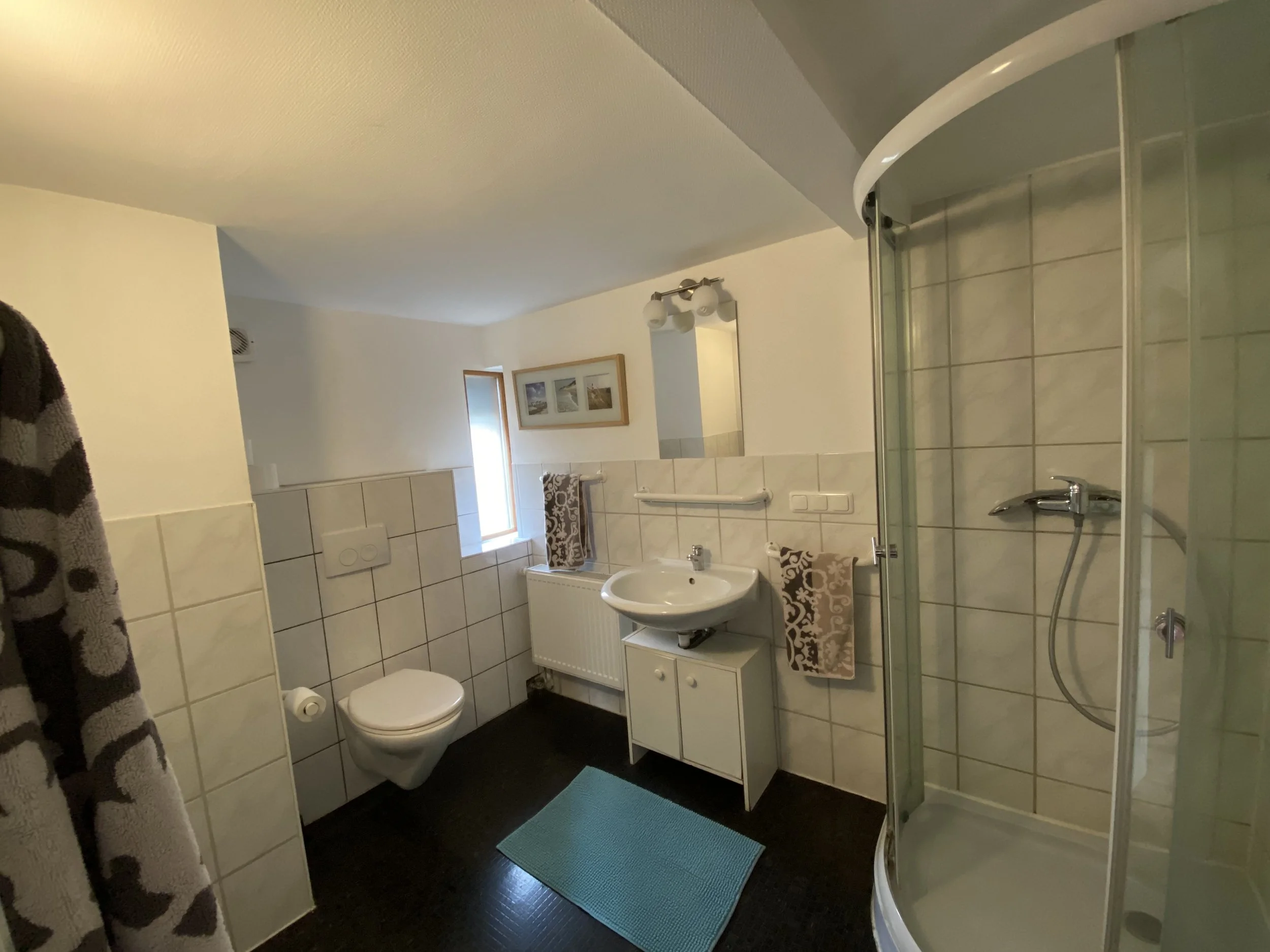 Badezimmer mit Toilette, Waschbecken, Spiegel, Dusche, Handtüchern und einem Fenster.