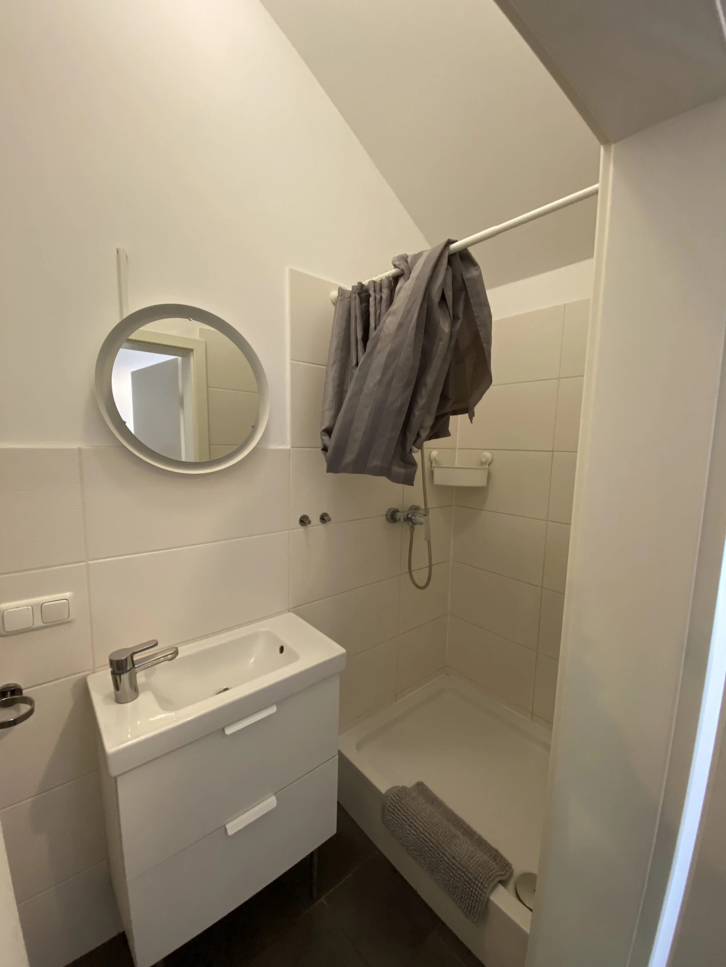 Kleines Badezimmer mit pointiertem Waschbecken, Spiegel und einer Dusche, die einen Vorhang zum Schutz vor Wasser hat.