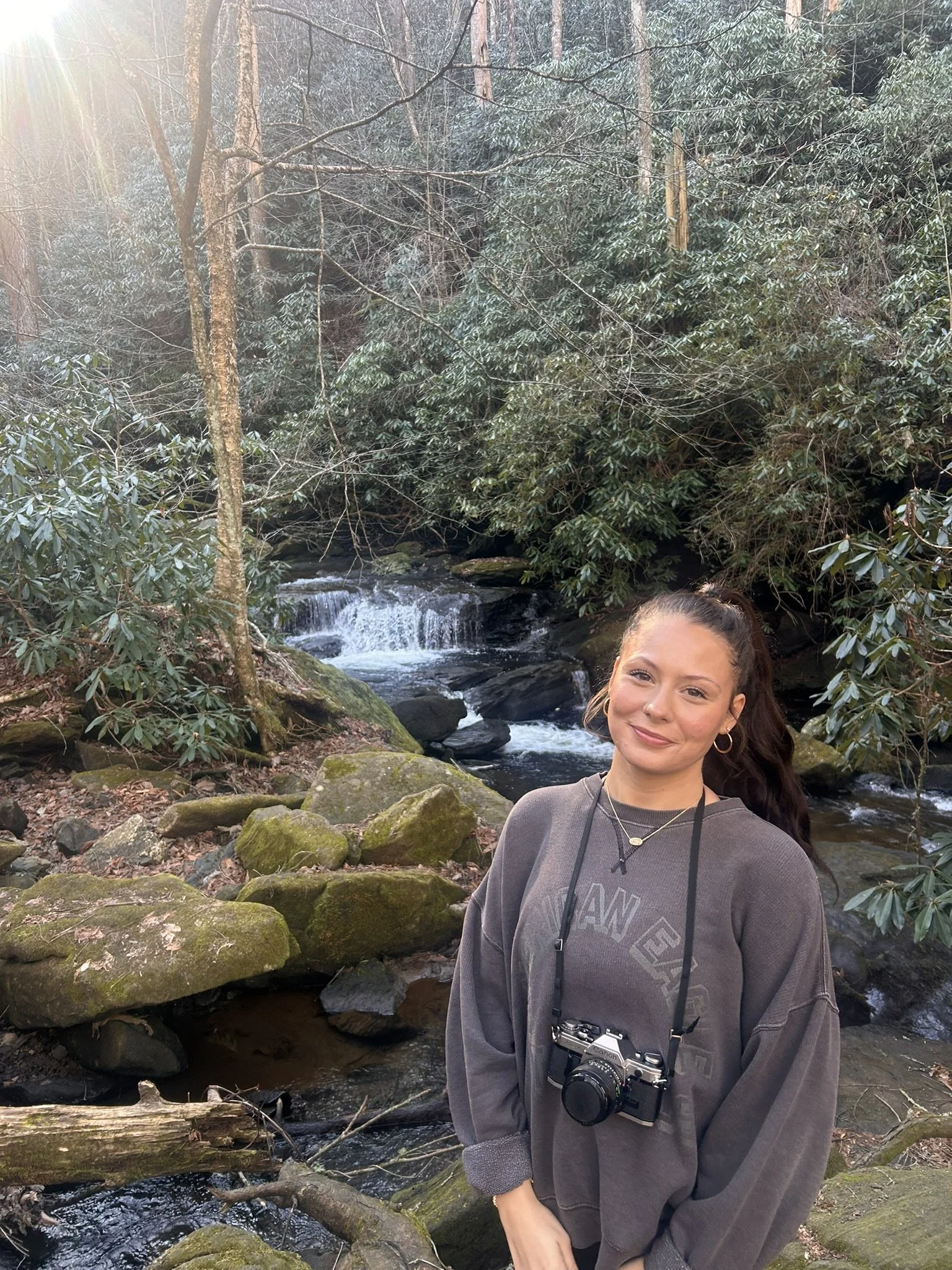 Alex Parks holding camera in front of small waterfall.