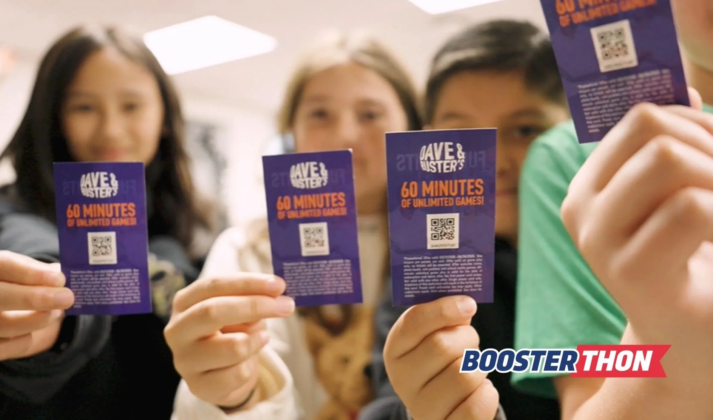 Three people holding promotional flyers for Dave & Buster's offering 60 minutes of unlimited games, with a background of an indoor setting.