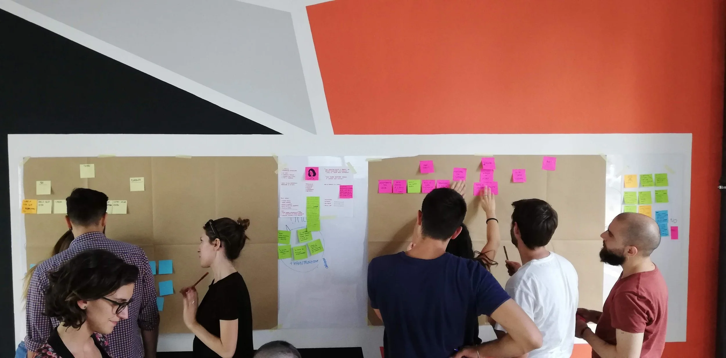 Gruppo di ragazzi e ragazze che collaborano attorno a un grande tabellone con post-it colorati, mentre discutono e prendono appunti in stile brainstorming.