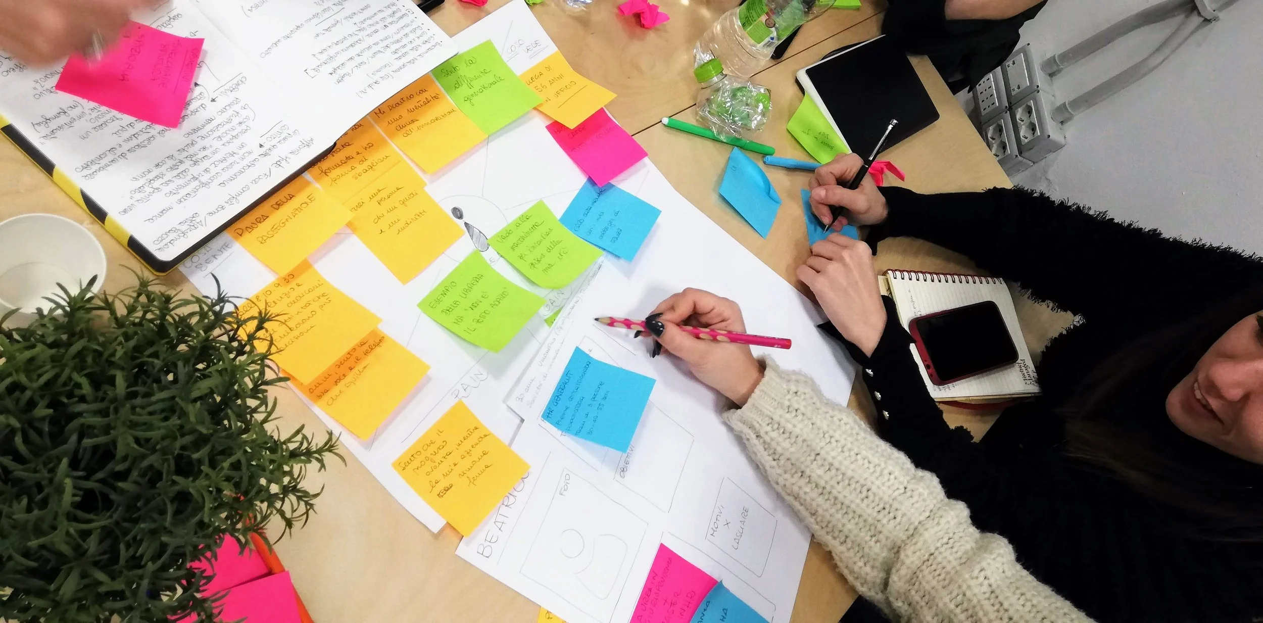 Due persone stanno facendo brainstorming su un tavolo con post-it colorati, appunti e strumenti di cancelleria, mentre condividono idee e discussioni.