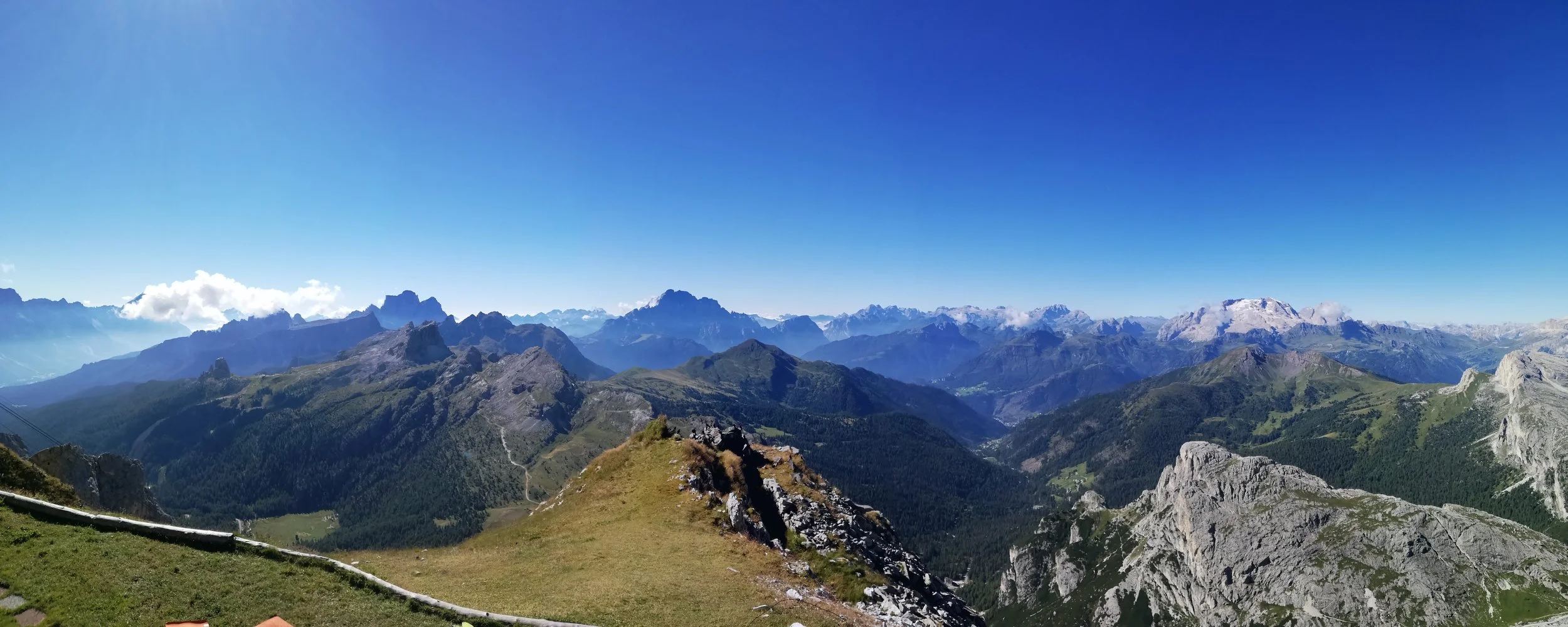 Panorama di montagne con cime innevate e vegetazione verde, sotto un cielo blu chiaro