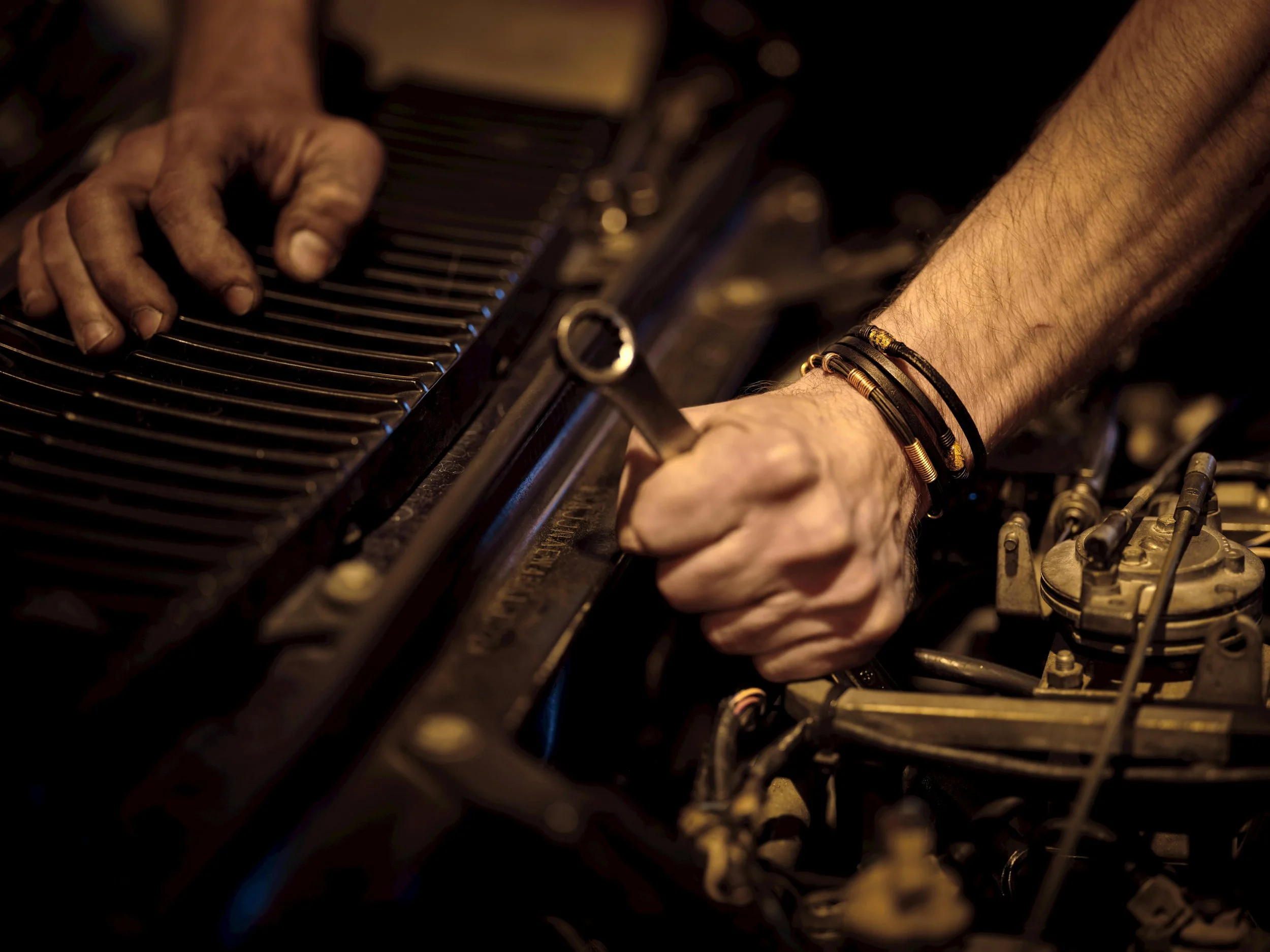 Close-up of a person's hands playing a vintage piano, adorned with multiple bracelets, in a dimly lit setting.