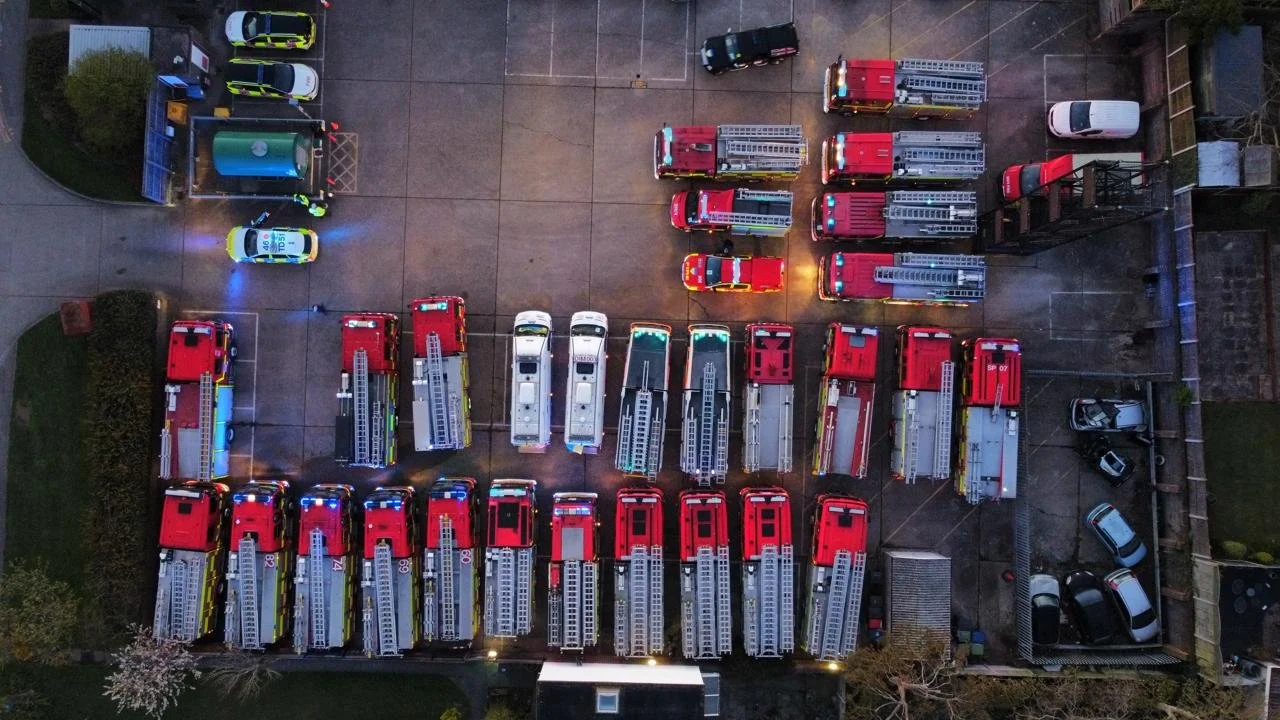 Aerial view of a parking lot with multiple fire trucks and emergency vehicles parked in rows.