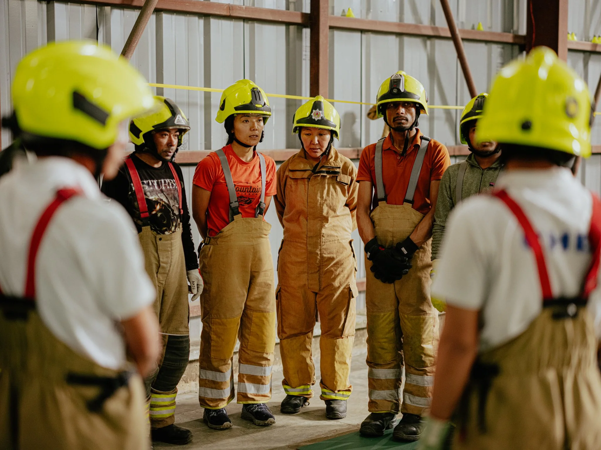 Firefighters in protective gear and helmets standing in a row inside a building, possibly during a safety briefing or inspection.