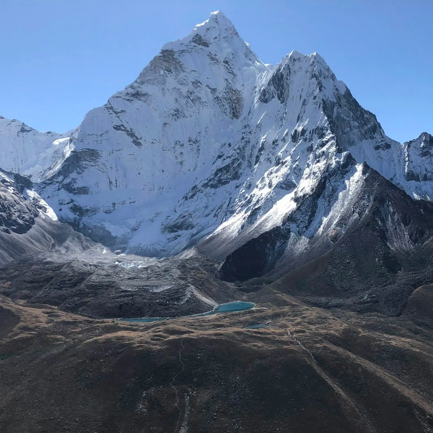 Snow-covered mountain range with a clear blue sky and small lakes in the foreground.