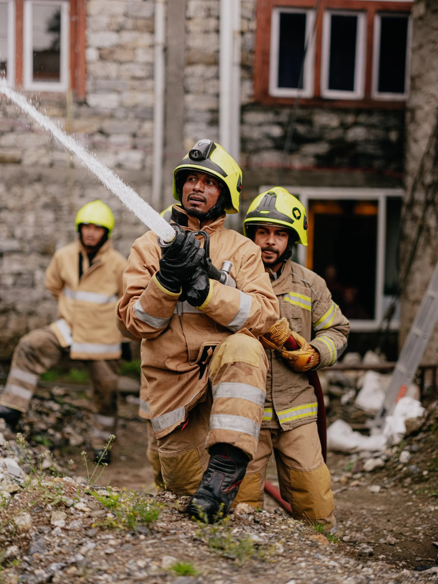 Firefighters in protective gear and helmets working at a disaster site with rubble and debris in the background.