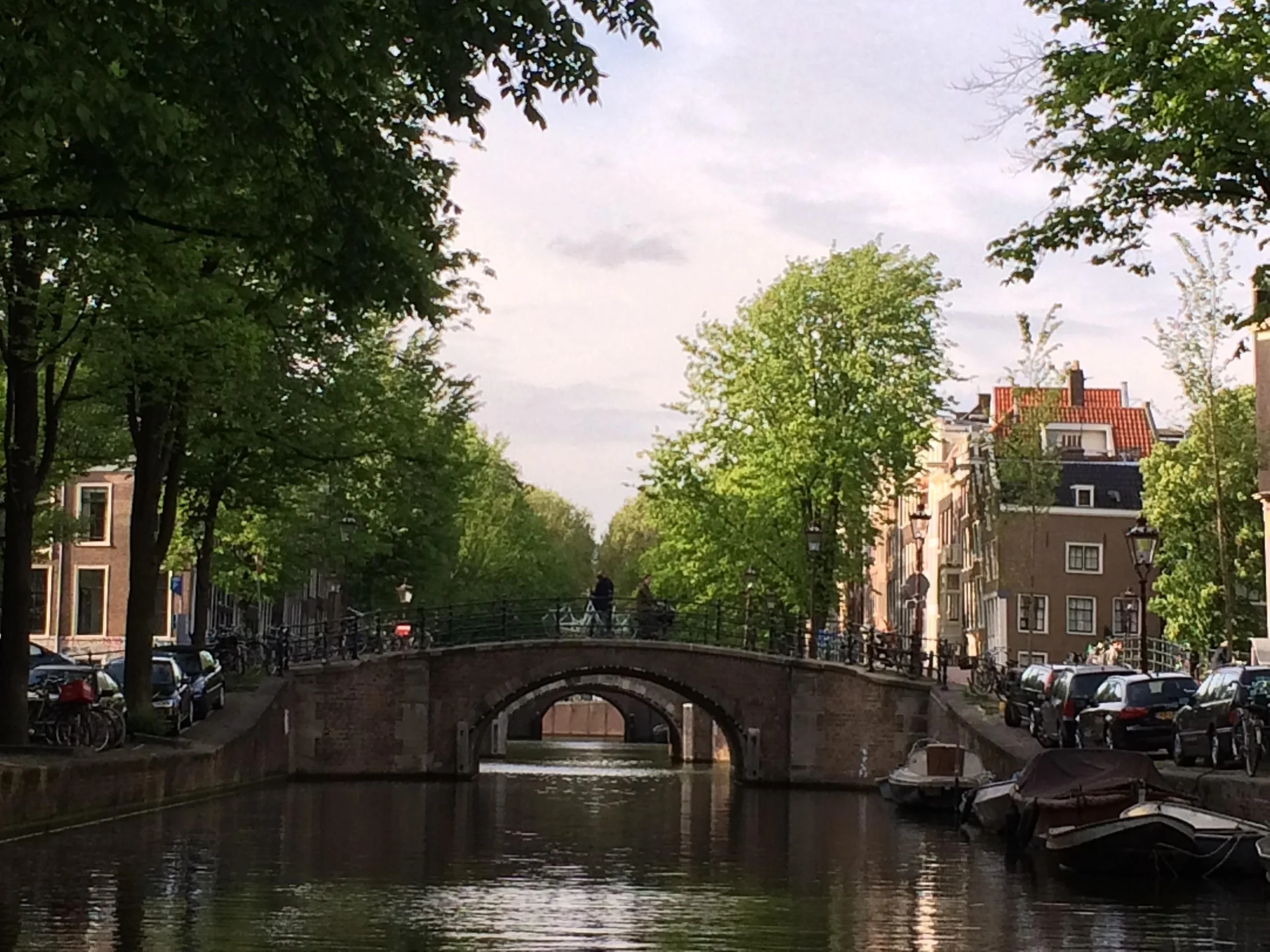 Een schilderachtig kanaal in Amsterdam met een voetgangersbrug en naastgelegen gebouwen, omringd door groene bomen en boten in het water.