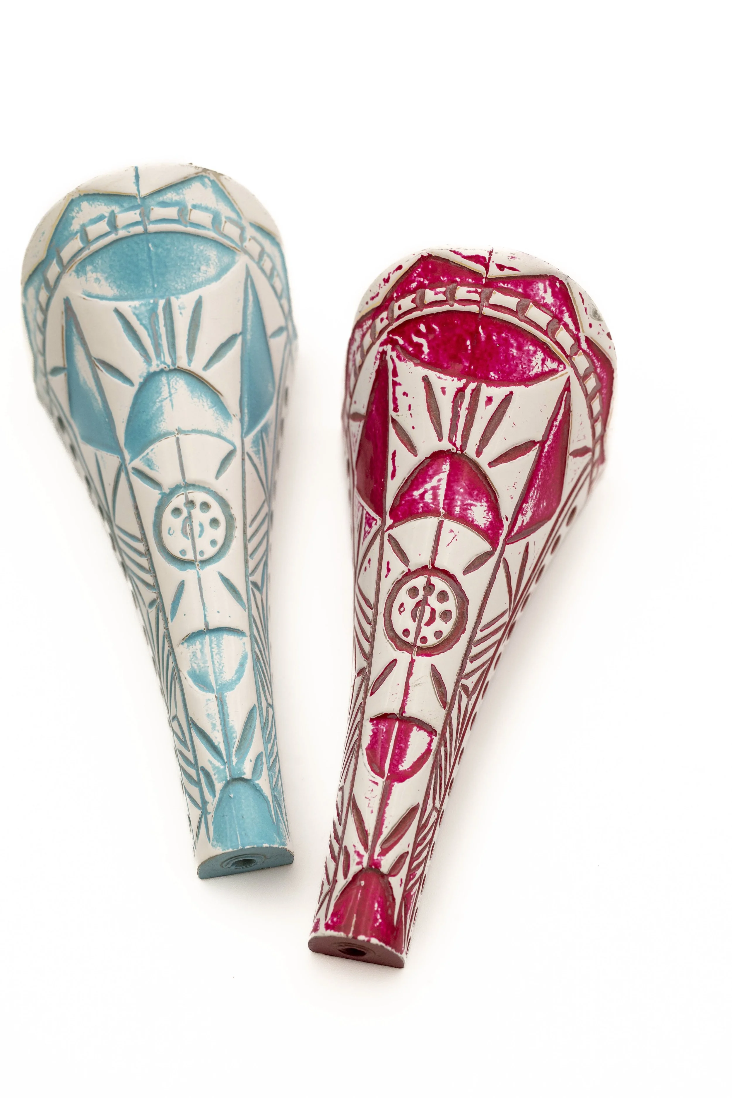 Dos molinillos de mano con patrones decorativos, uno en tono azul y otro en rosa, colocados sobre un fondo blanco.