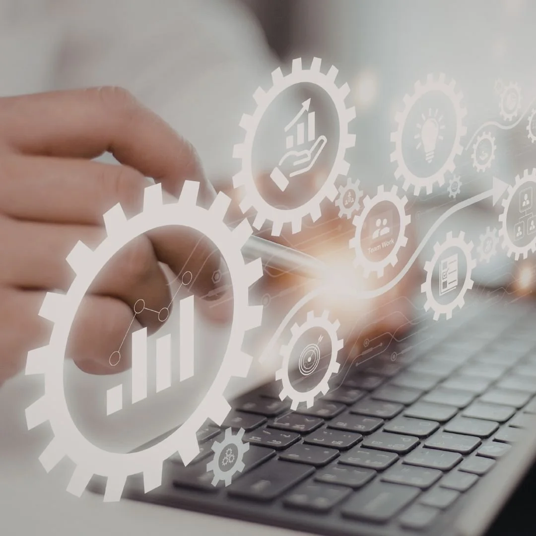 Mano tocando una pantalla digital con íconos de engranajes, gráficas, y conceptos como innovación, trabajo en equipo, y crecimiento, sobre un teclado de computadora.