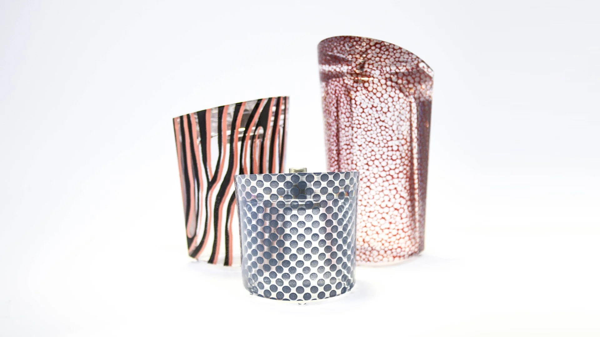 Tres vasos decorativos con patrones diferentes en colores rojos, azules y negros sobre fondo blanco.