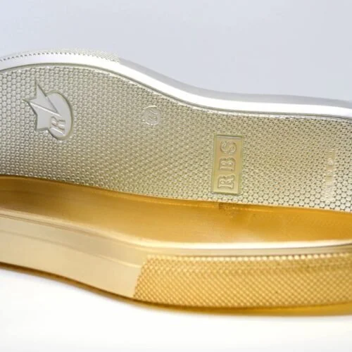 Parte inferior de un zapato lustrado con detalles en dorado y marca RB en la suela.