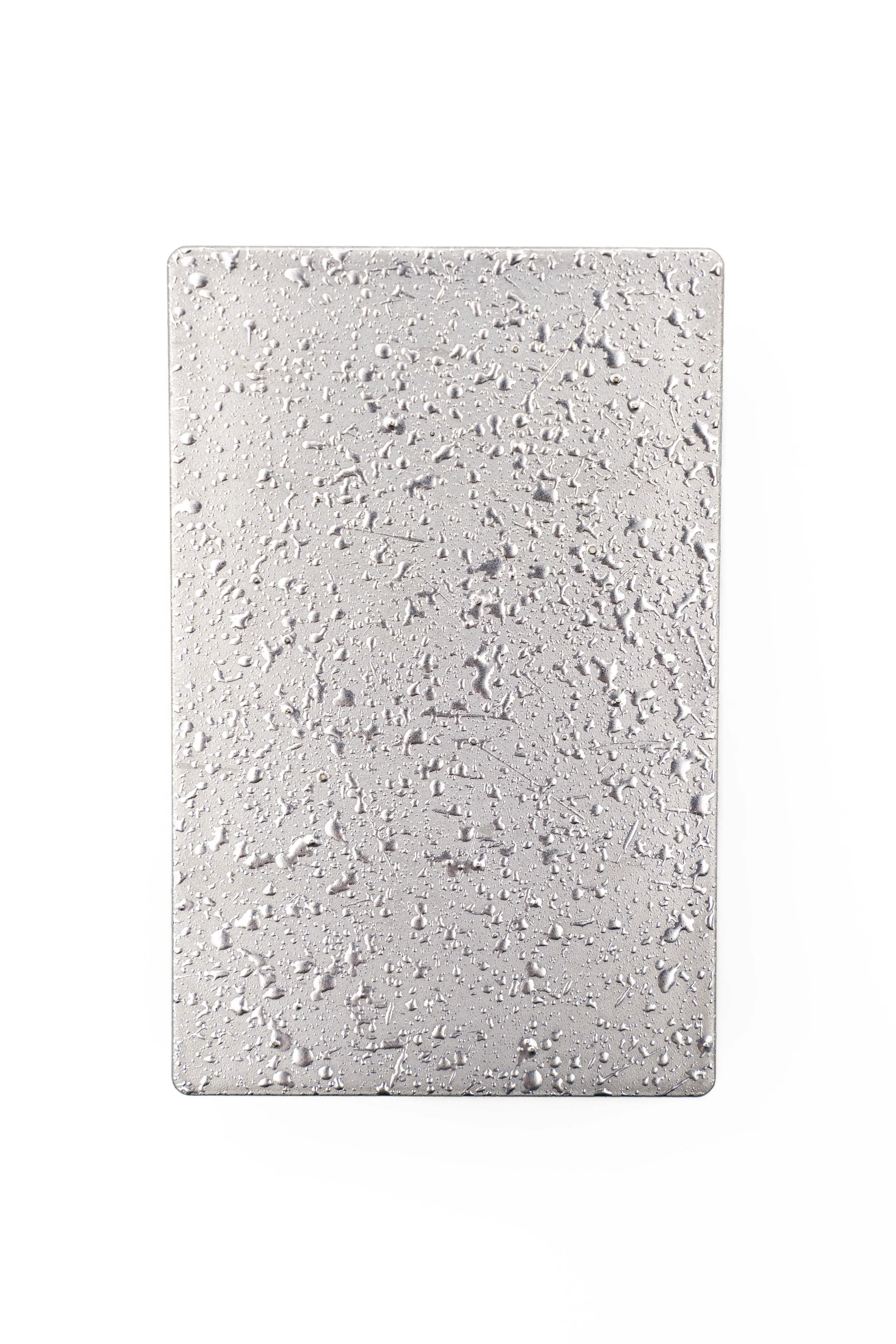 Superficie de metal con gotas de agua sobre ella, con fondo blanco.