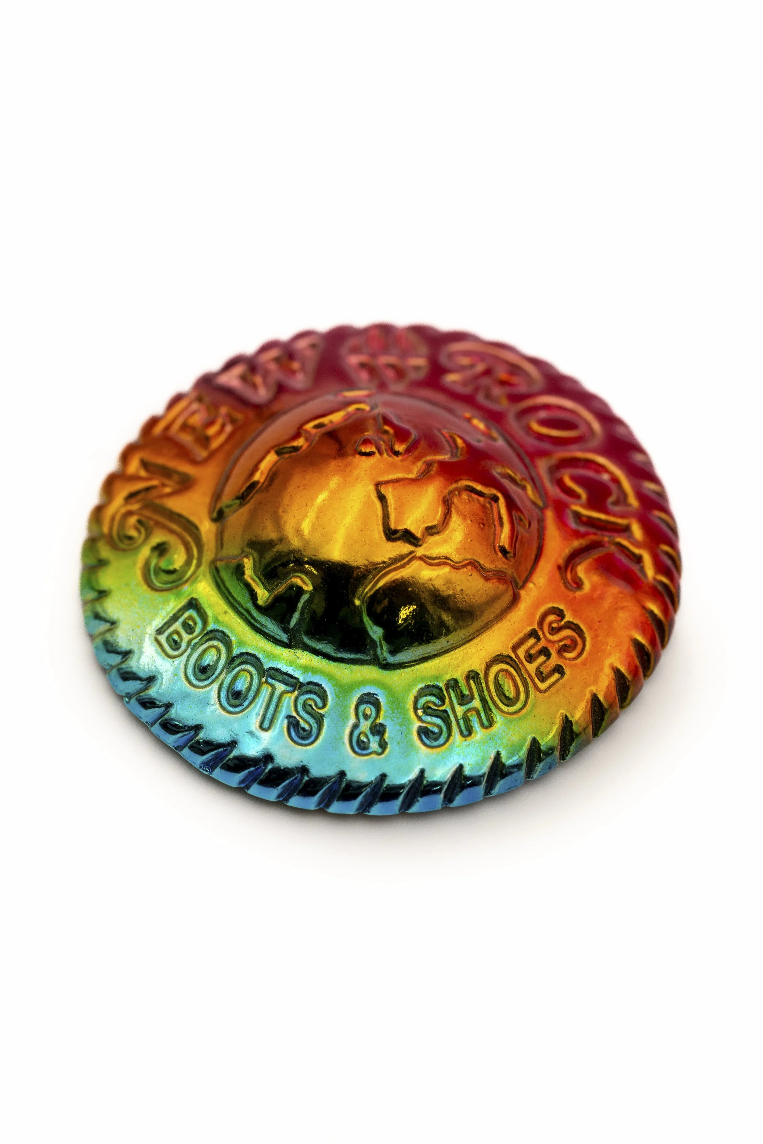 Una medalla con efectos de arcoíris, que tiene un diseño de un rostro en el centro y letras que dicen 'BOOKS & SHOTS' alrededor.