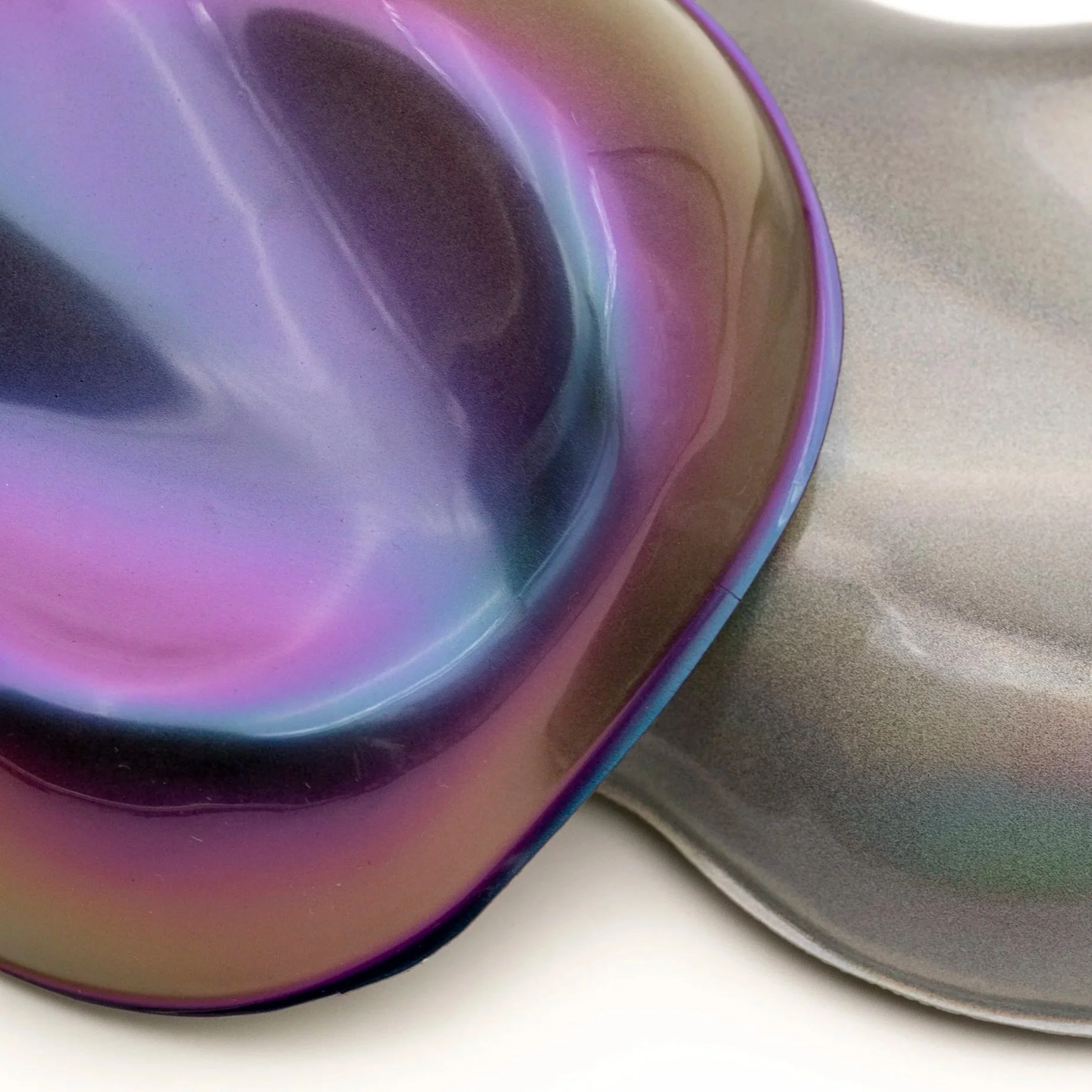 Se muestran varias tazas de cerámica con un acabado iridiscente en tonos violeta, dorado y plateado, colocadas en una superficie blanca y gris.