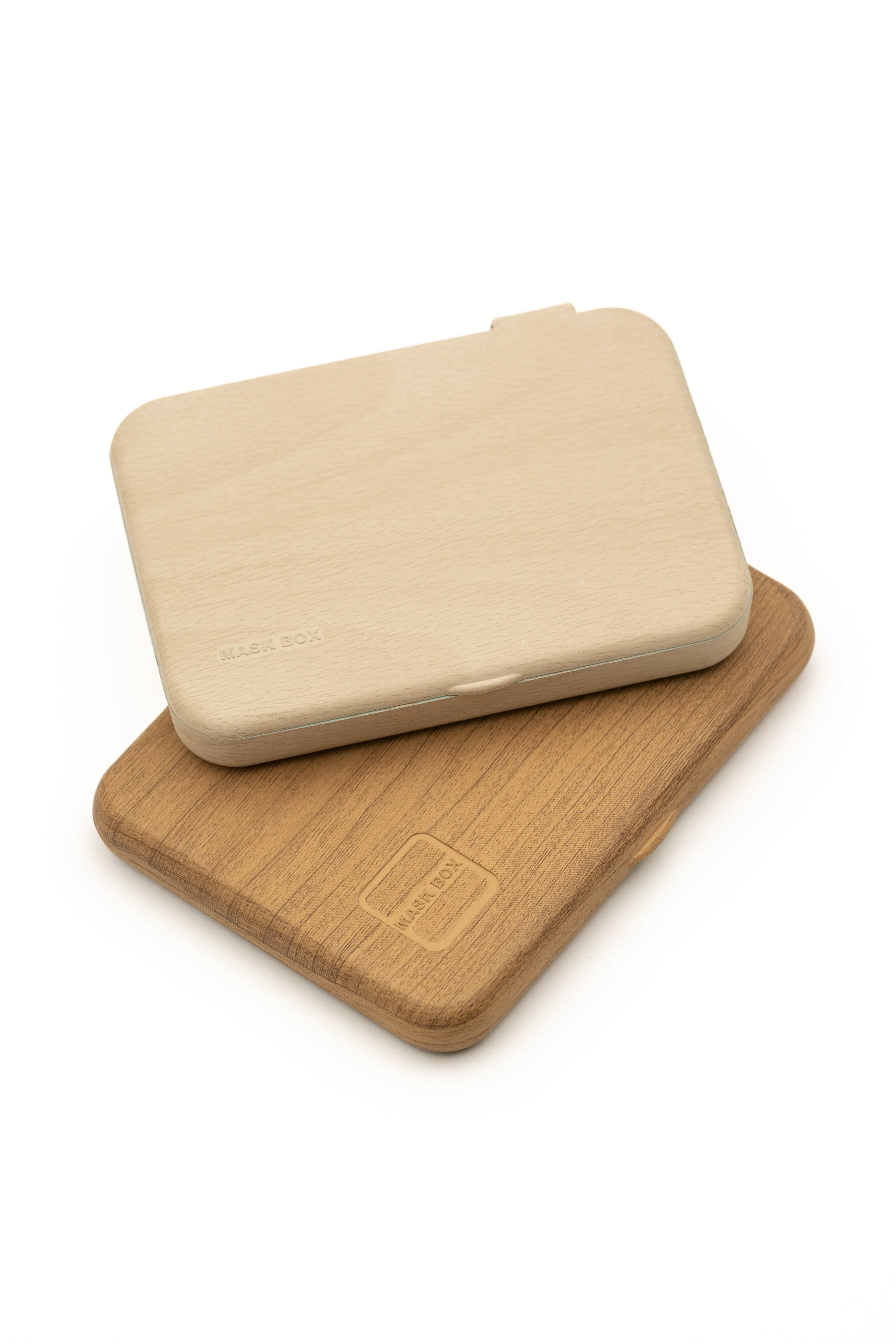 Tres cajas de mascarillas de diferentes colores y materiales, apiladas unas sobre otras, con la caja superior en color madera clara, la del medio en color madera media y la inferior en color madera oscura.