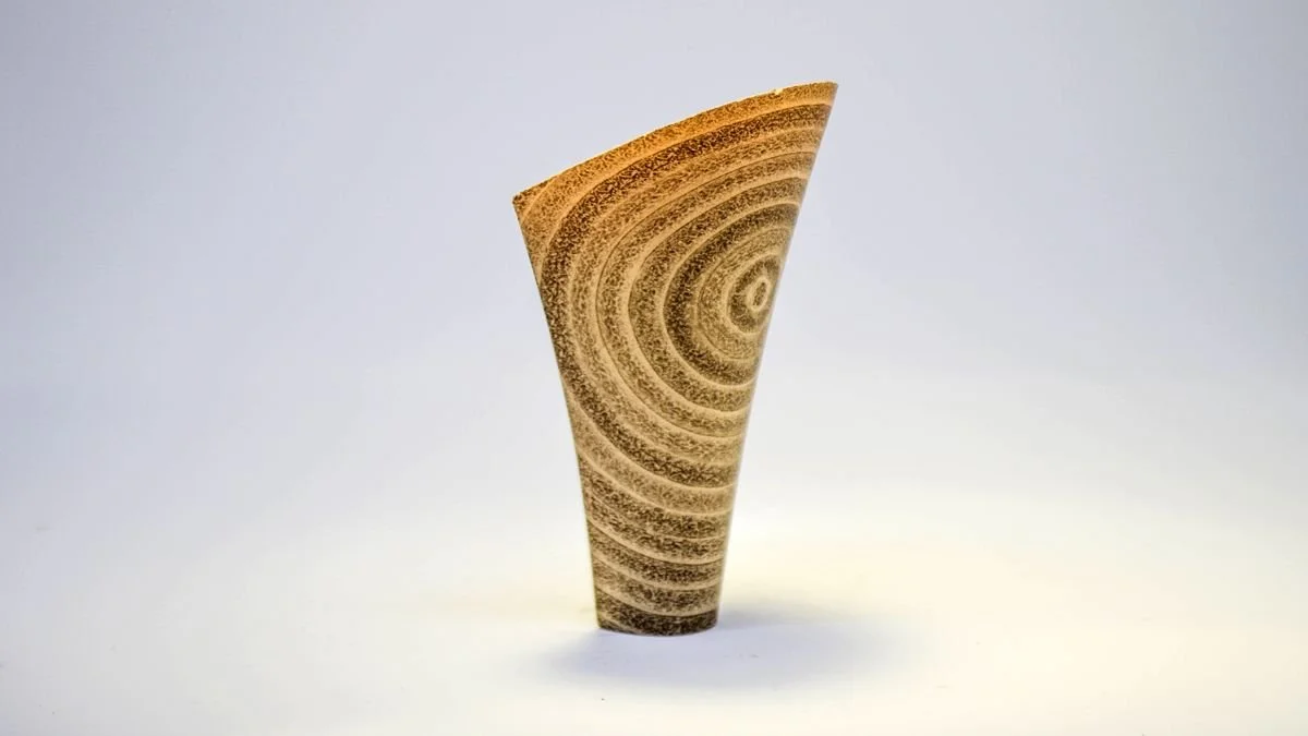 Escultura de barro con patrones circulares en tonos marrones y beige.