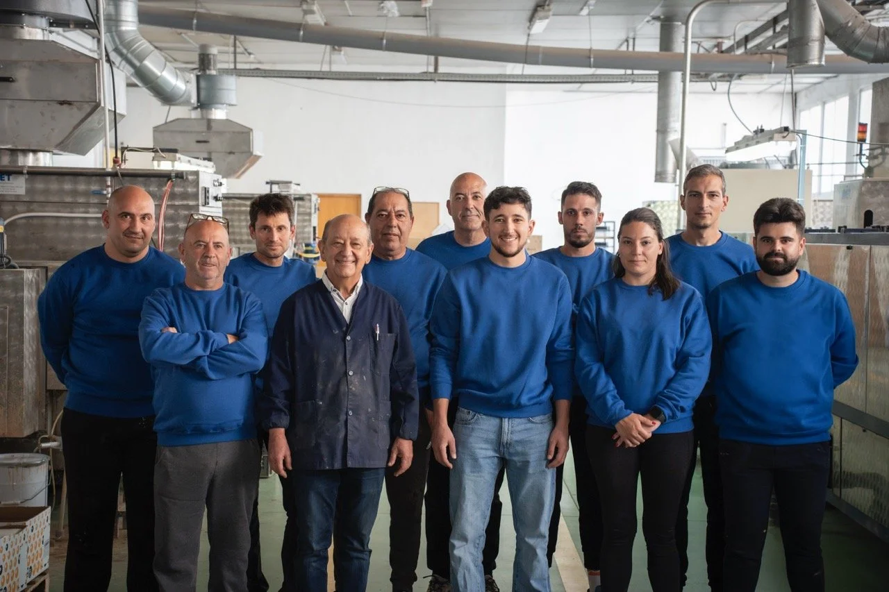 Grupo de personas en un entorno de fábrica o laboratorio, todos con ropa azul, algunos con gafas en el cabello, posando para una foto grupal.