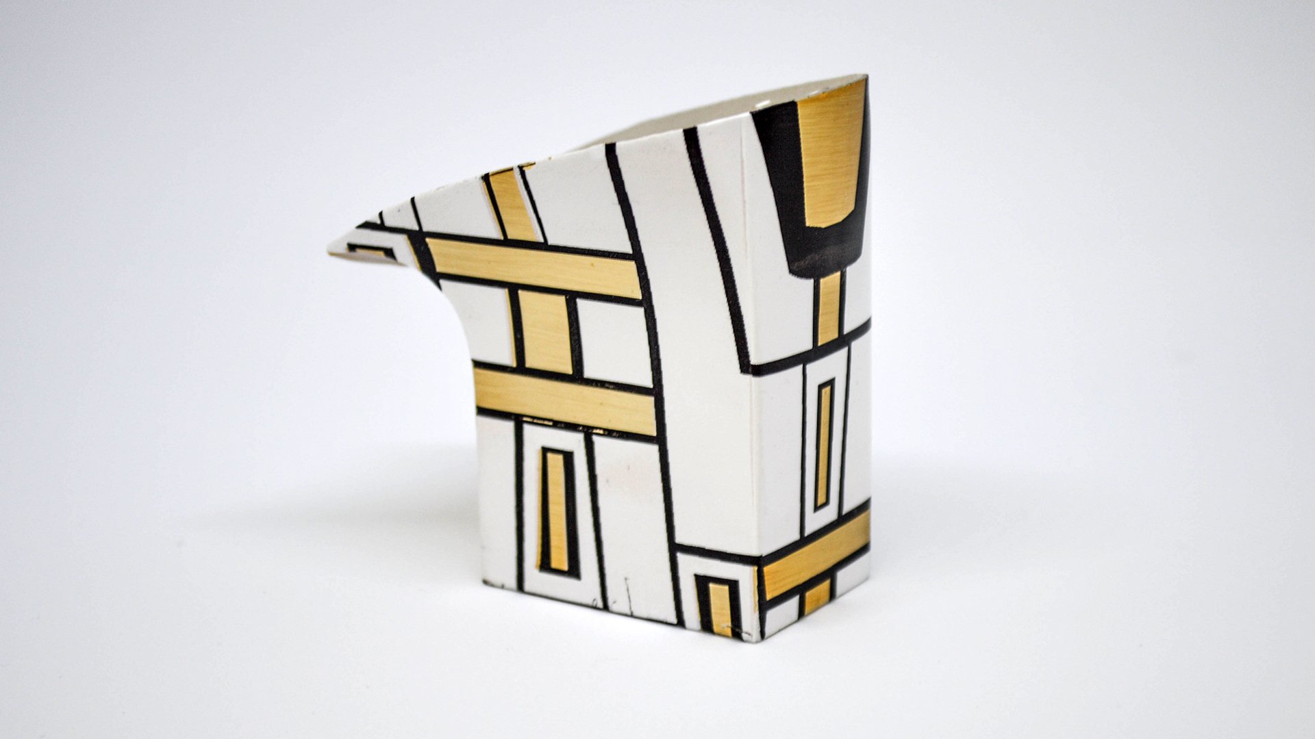 Vaso decorativo con diseño geométrico en colores blanco, negro y dorado, de forma prismática con una punta afilada.
