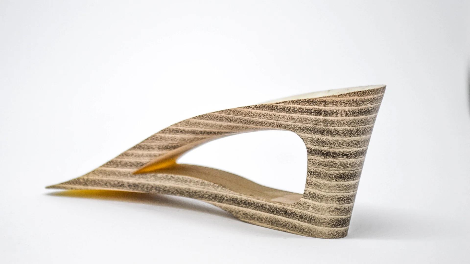 Zapato de tacón hecho de madera con diseño de líneas curvas y texturas naturales, colocado sobre fondo blanco.