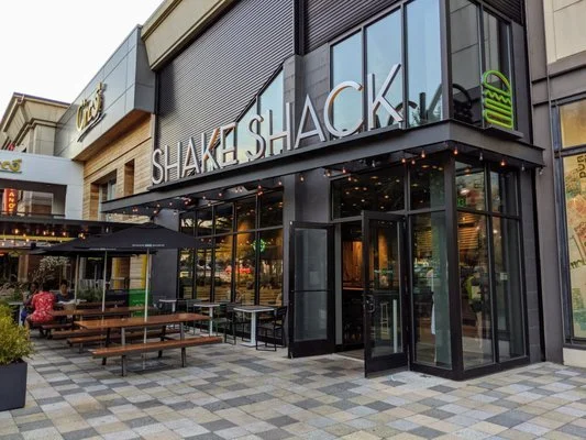 Exterior of a Shake Shack restaurant with outdoor seating and glass storefront.