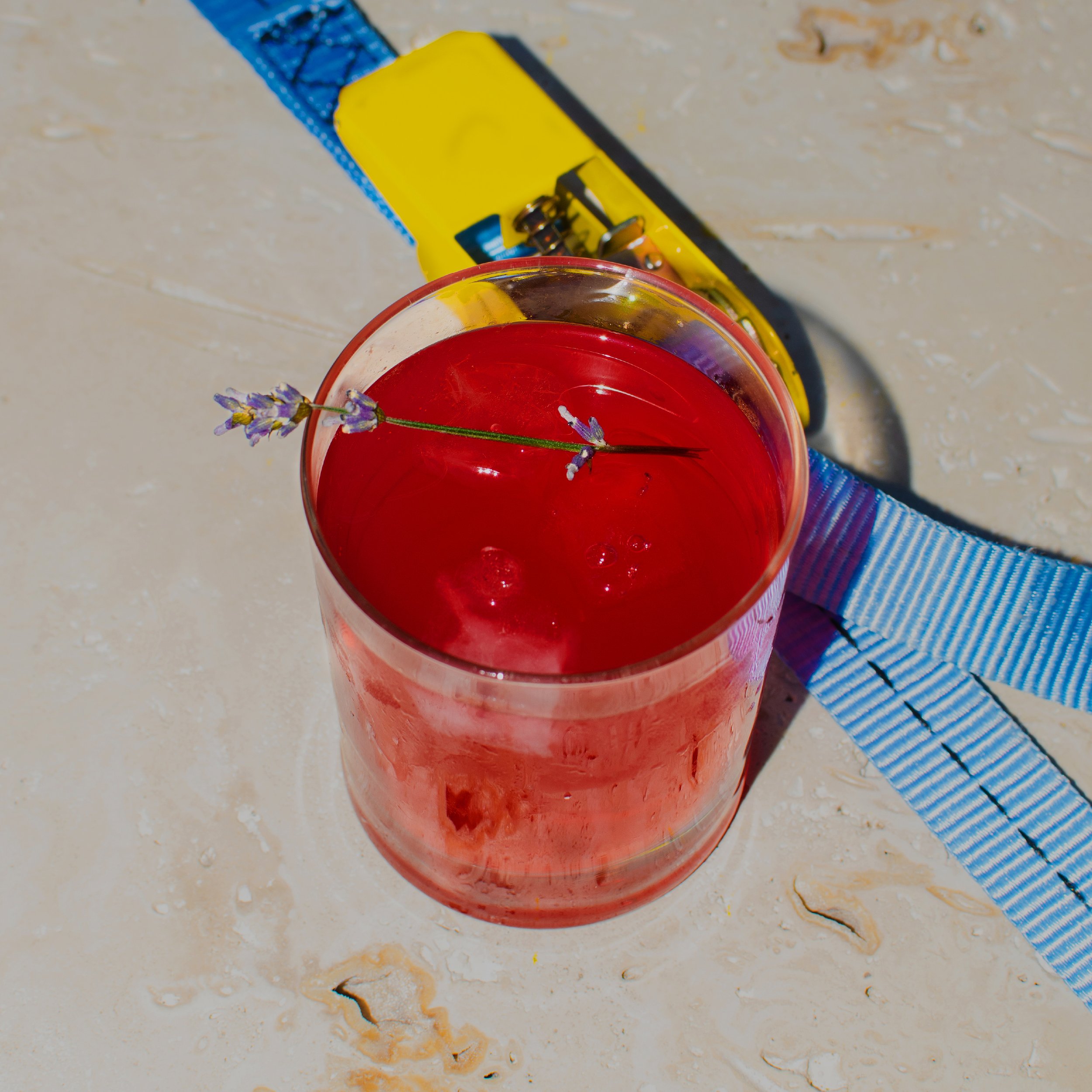 Rotes CHerry Getränk in einem transparenten Glas mit Lavendelzweig darauf, auf einem Marmorblock