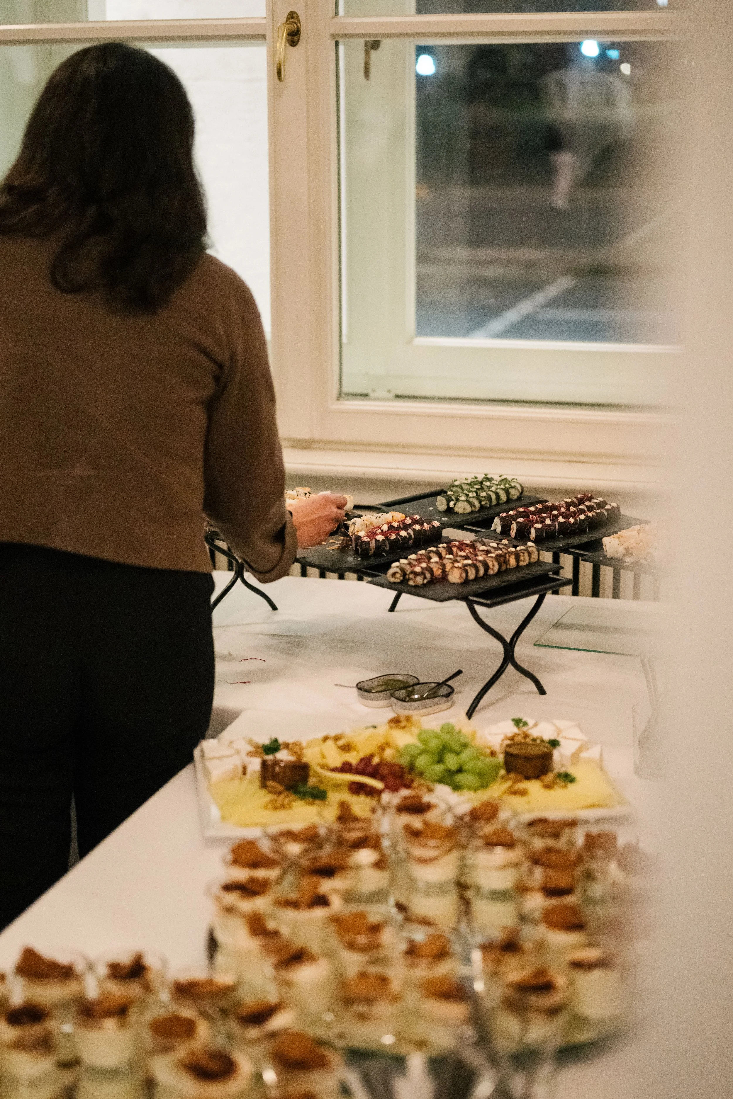Eine Frau bedient eine Dessert-Bar mit verschiedenen Torten und Süßigkeiten bei einer Feier im Innenbereich.