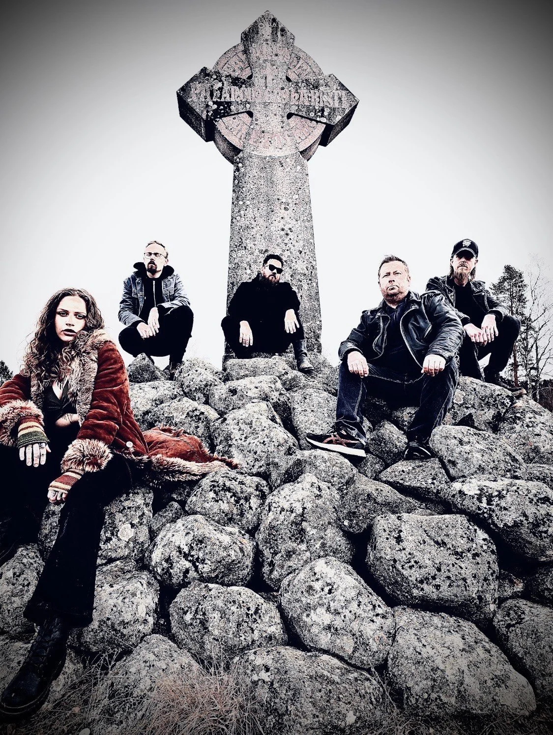 Five people sitting on rocks in front of a large cross monument against a cloudy sky.