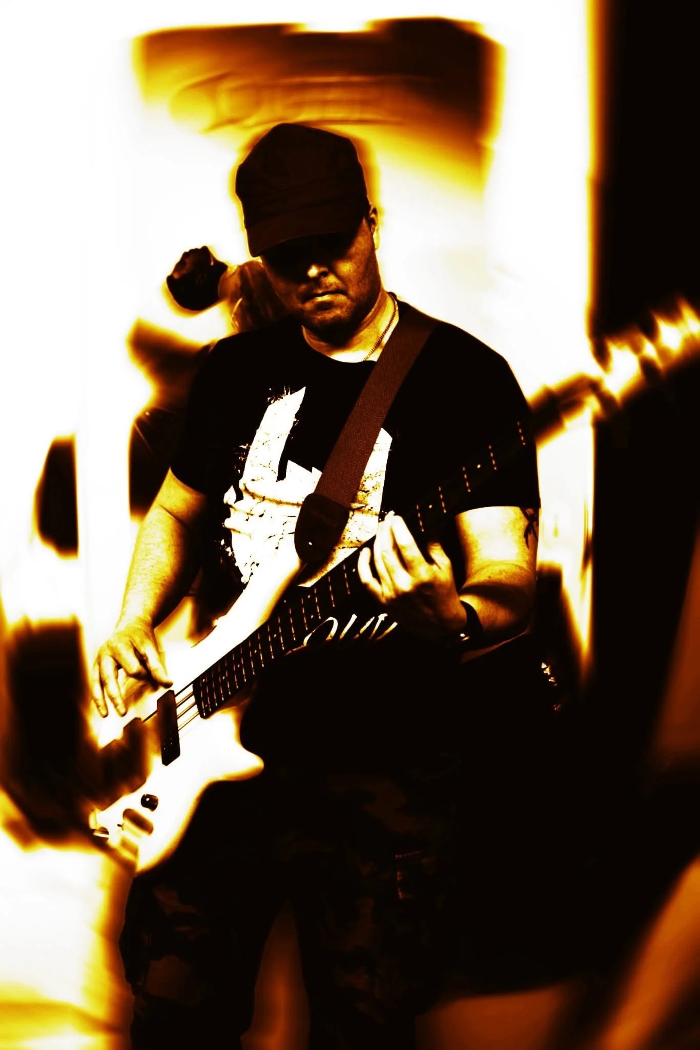 A man wearing a black cap and sunglasses playing an electric guitar with a glowing background.