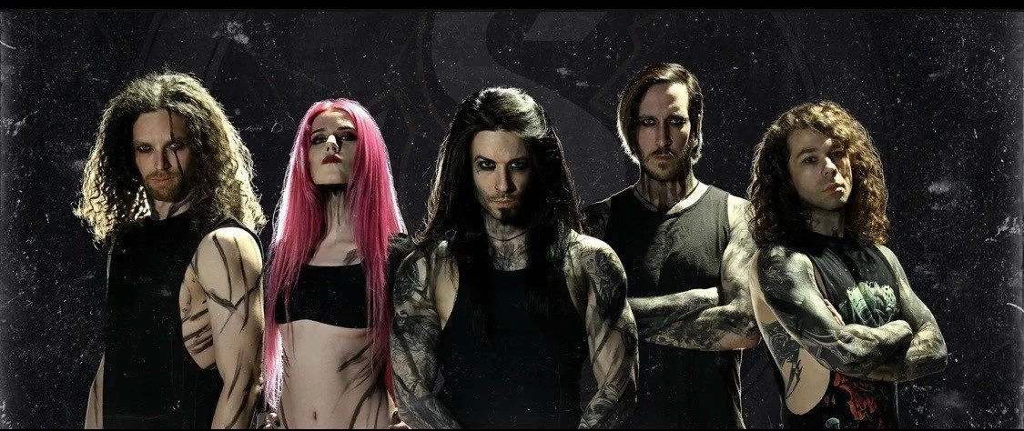 Six members of a metal band with long hair and tattoos, standing with arms crossed against a dark, textured background.