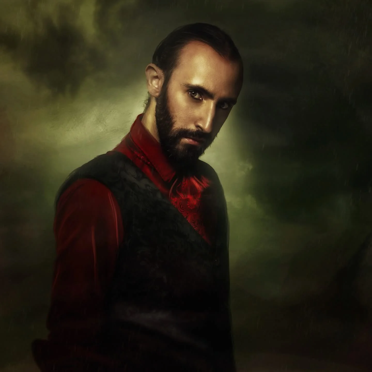 A man with dark hair and beard wearing a dark and red kurta, looking at the camera against a dark greenish background.
