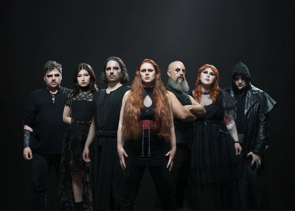 Group of seven people dressed in black gothic and alternative fashion posing against a dark background.
