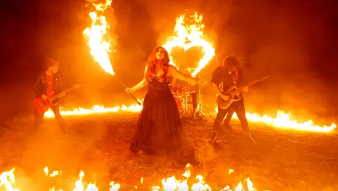 A band performing on a stage surrounded by fire and large flames during a concert or show.
