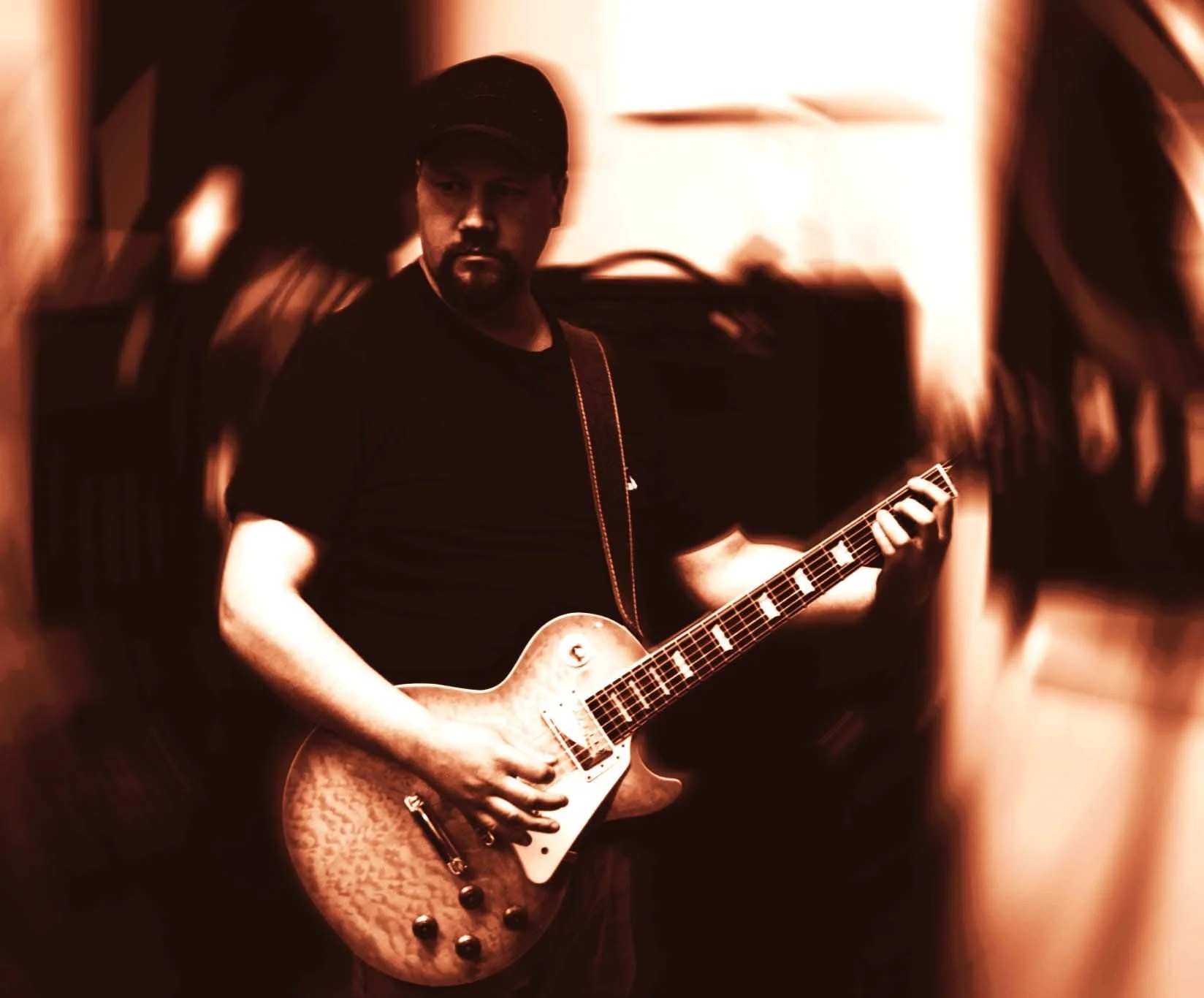A man playing an electric guitar in a dimly lit room with warm tones.