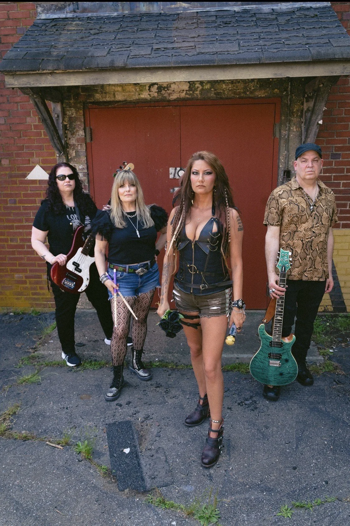 Four musicians standing in front of a brick building with a red door, holding musical instruments.