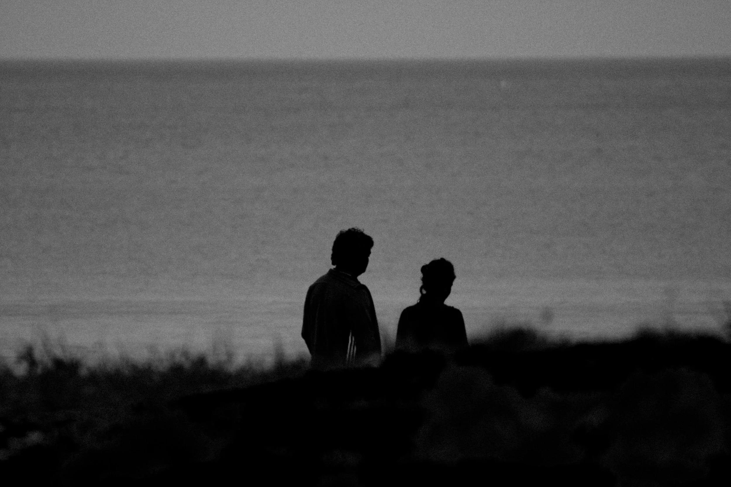 Silhouettes of two people standing outdoors at dusk or dawn with a cloudy sky in the background