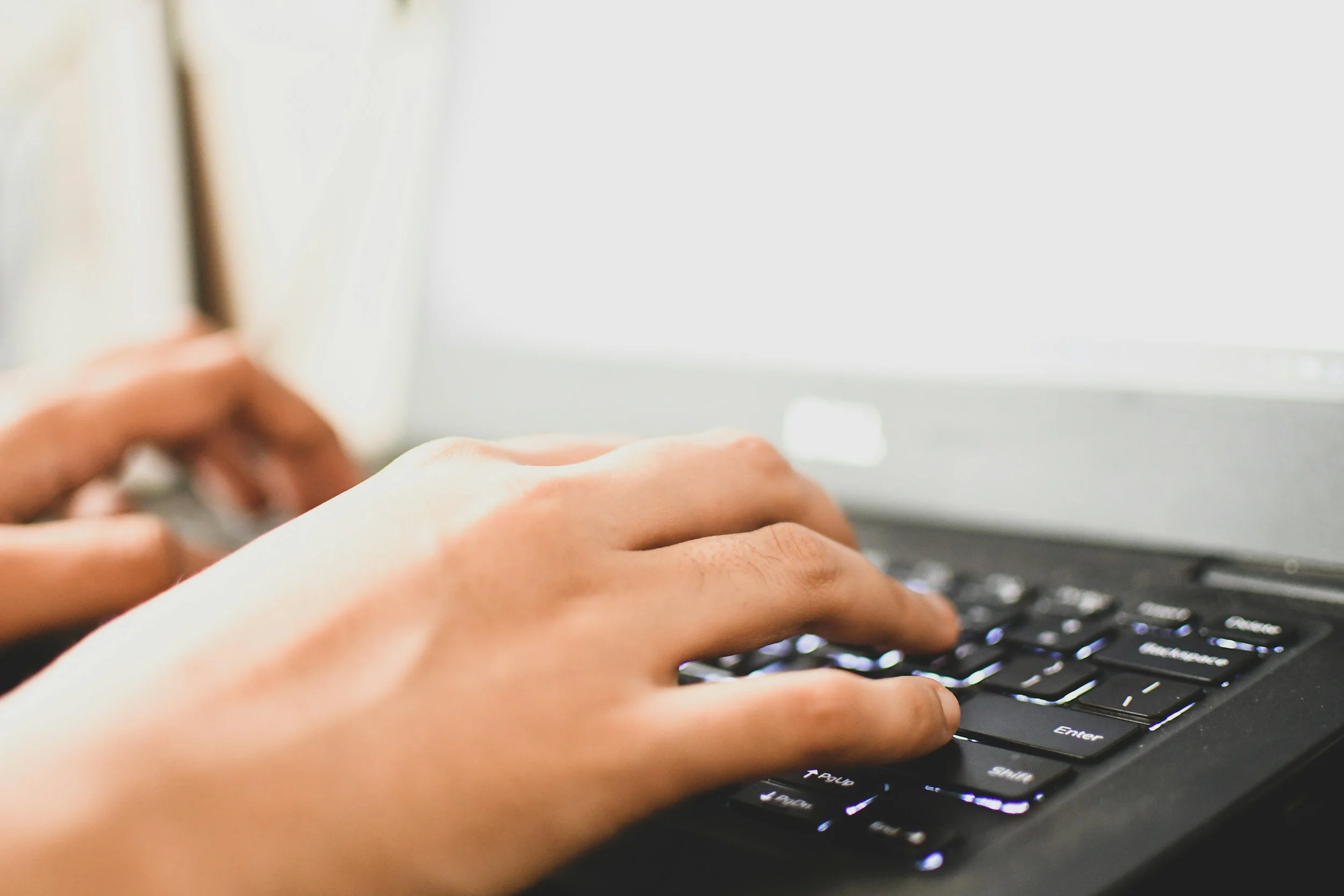 Close-up of hands typing on a black computer keyboard.