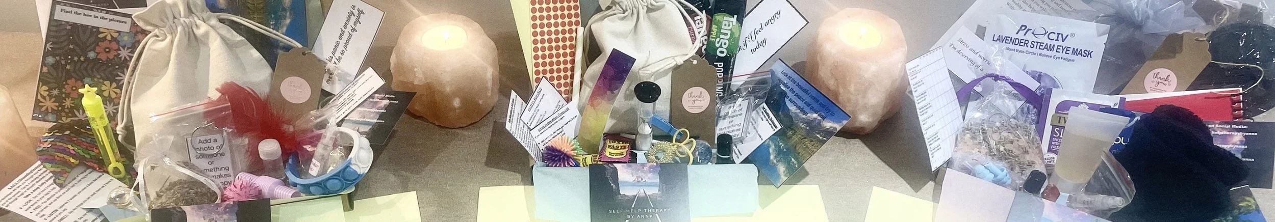 A tabletop display of various self-care and wellness items, including candles, skincare products, essential oils, and informational pamphlets, arranged with some candles lit.