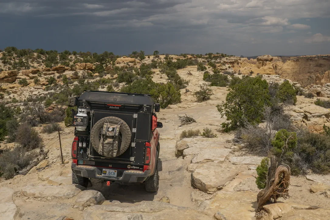 image of the back of a camper truck driving rough rock terrain with a dark cloud storm overhead