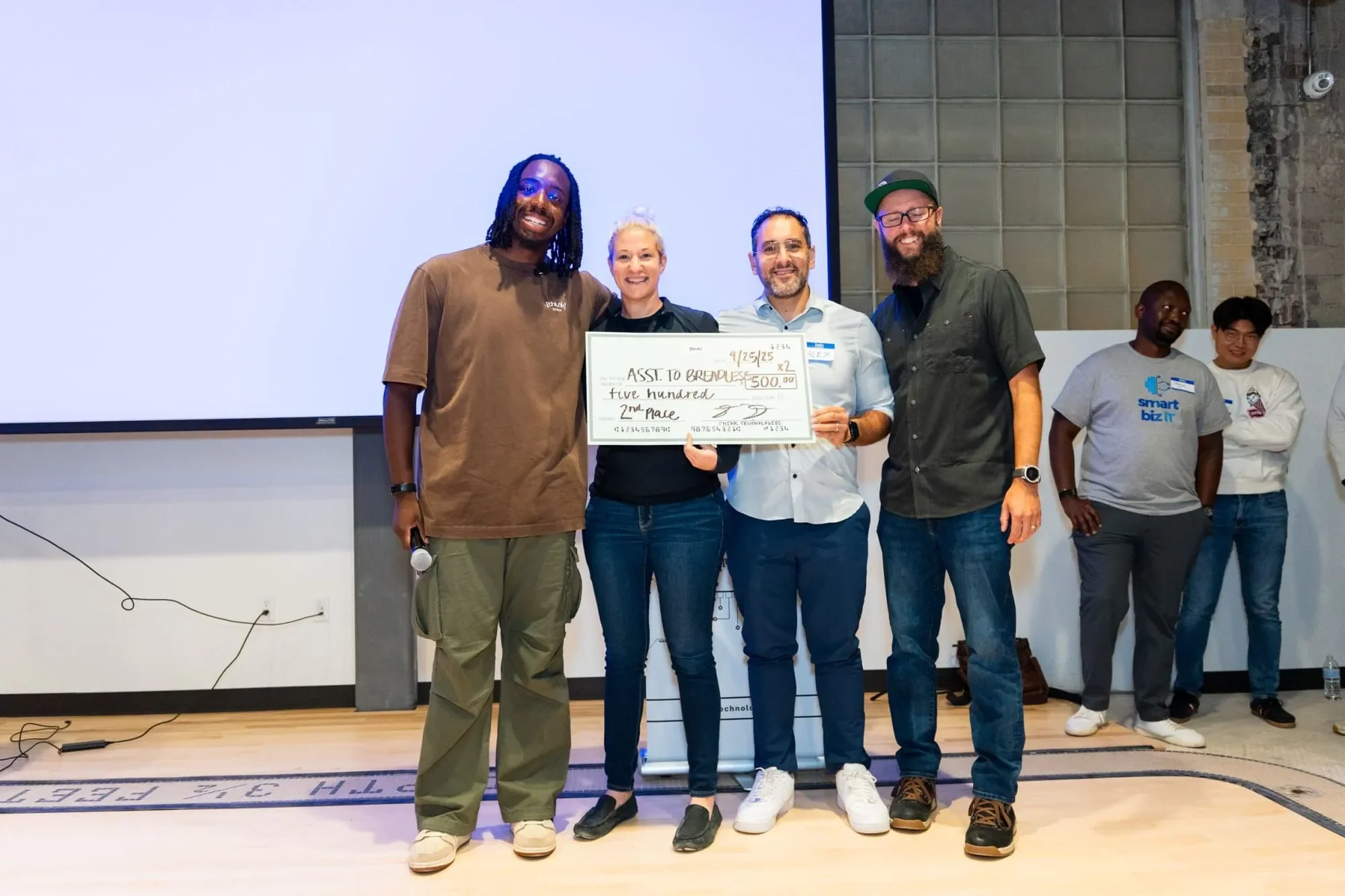 image of four individuals standing on a stage with a large check written out to the second place hackathon team